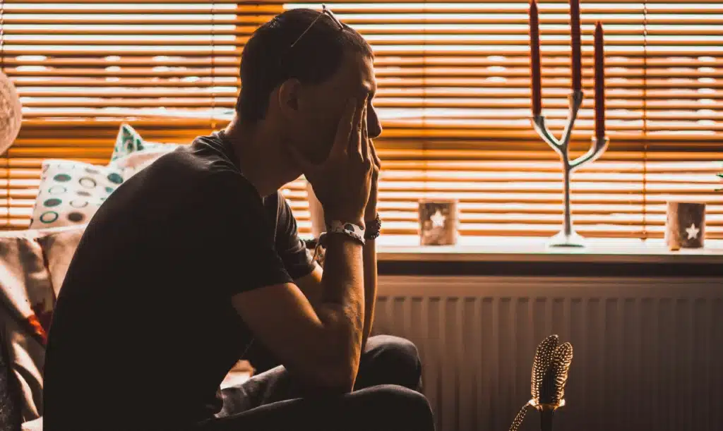 Silhouette of a man sitting in a room with blinds, appearing thoughtful or stressed